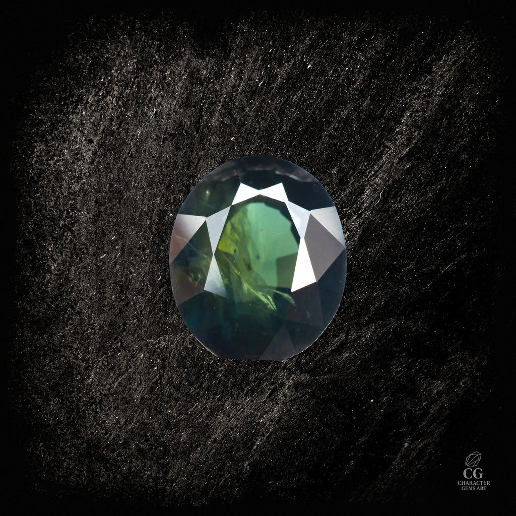 Blauer Saphir von Character Gemstones, 2,19 Karat, mit grünlichem Obsidian-Hintergrund, detailreiche Edelsteinaufnahme.