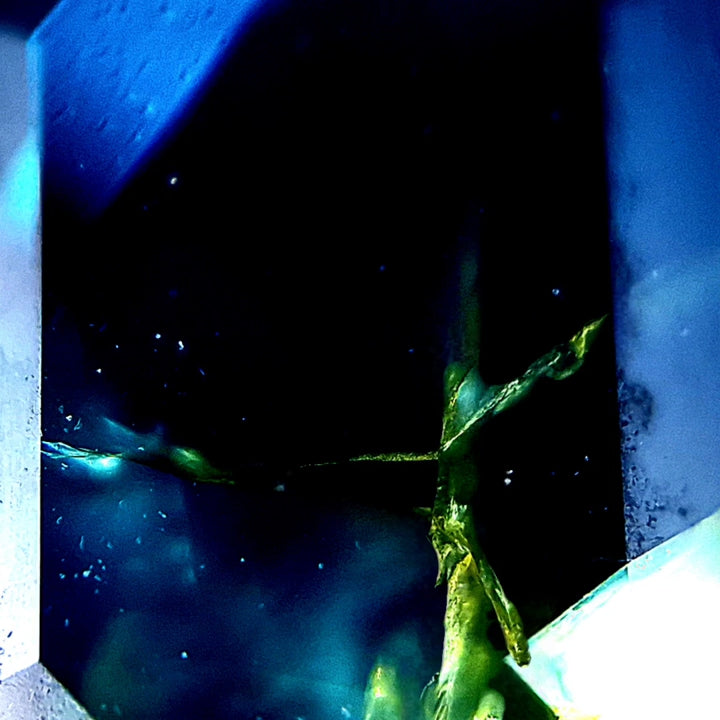 Makrofoto goldener Kristallkörper in einem unbehandelten Parti-Saphir, wirkt wie in einer fernen Galaxie